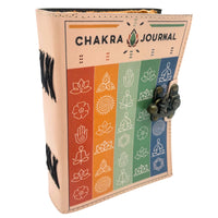 Cuaderno de cuero de 7 Chakras de 12,5x17,5cm, visto en ángulo, mostrando la portada con diseño de franjas de colores que representan los chakras y sus símbolos asociados. Lleva las palabras 'CHAKRA JOURNAL' en la parte superior y un cierre metálico de estilo antiguo. Perfecto para terapias, yoga o registro espiritual