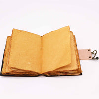 Cuaderno de cuero de 7 Chakras de 12,5x17,5cm abierto, mostrando sus páginas rústicas de papel artesanal en tono dorado. Cuenta con encuadernación visible y un cierre de cuero con gancho, ideal como diario, libro de bocetos o para prácticas espirituales